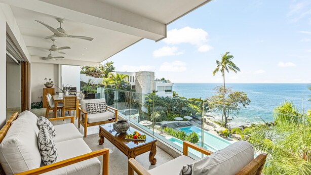 Un balcon avec vue sur l’océan, aménagé avec un canapé, des fauteuils et une table sur laquelle se trouve un saladier rempli de fruits.