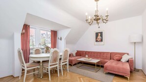 A dining area with a round table and chairs, a pink sofa, and a chandelier. - Lumina Apartments for family in the Old Town (Warszawa BIG)
