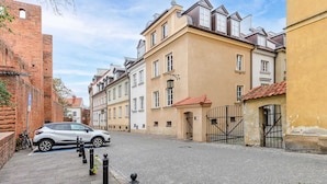A cobblestone street lined with historic buildings, a parked car, and bollards along the sidewalk. - Lumina Apartments for family in the Old Town (Warszawa BIG)