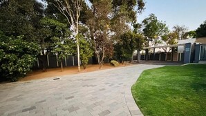 A paved walkway with a grassy area on one side and a building entrance with a covered walkway in the background. - Rolem Guest House (Randburg)
