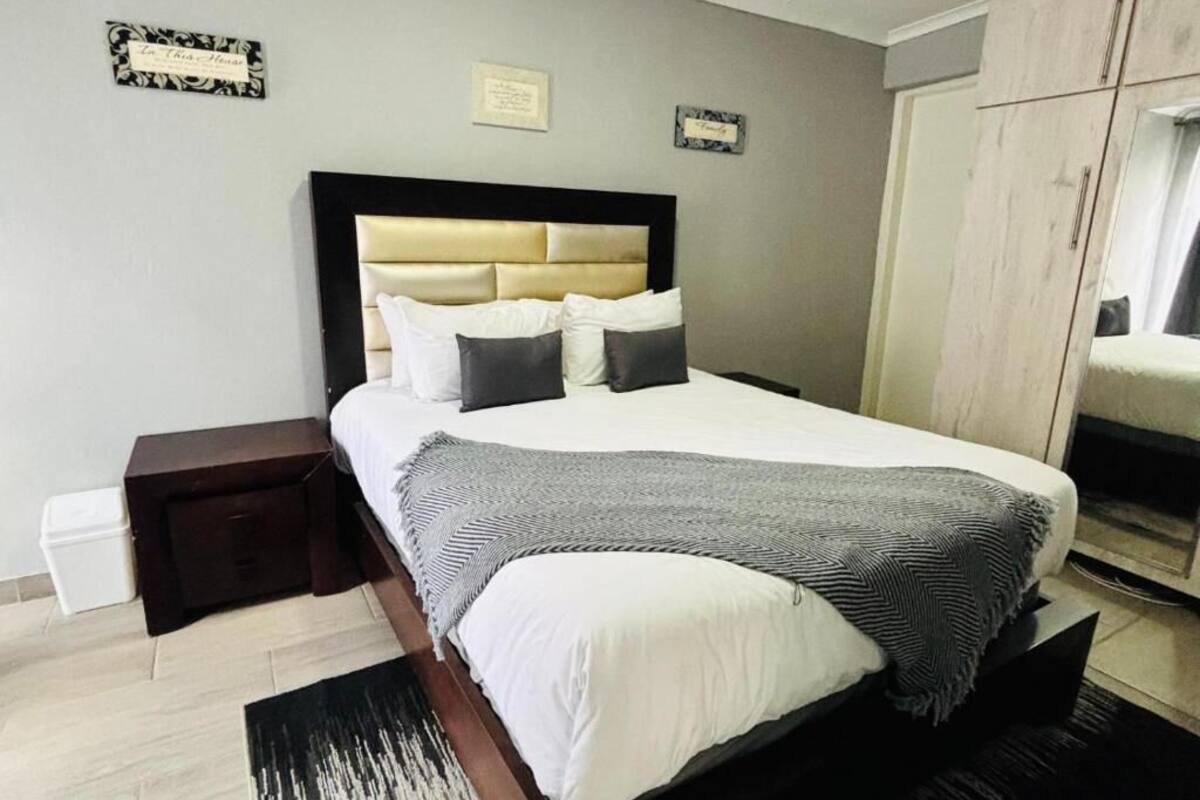 A neatly made bed with a headboard, a bedside table, a wardrobe, and a small trash bin.