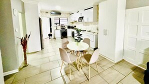 A modern kitchen with white cabinets, a dining area with a round table and four chairs, and a hallway leading to another room. - Rolem Guest House (Randburg)