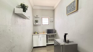 A compact kitchen with white cabinets, a microwave, a coffee machine, and a small window. - Rolem Guest House (Randburg)