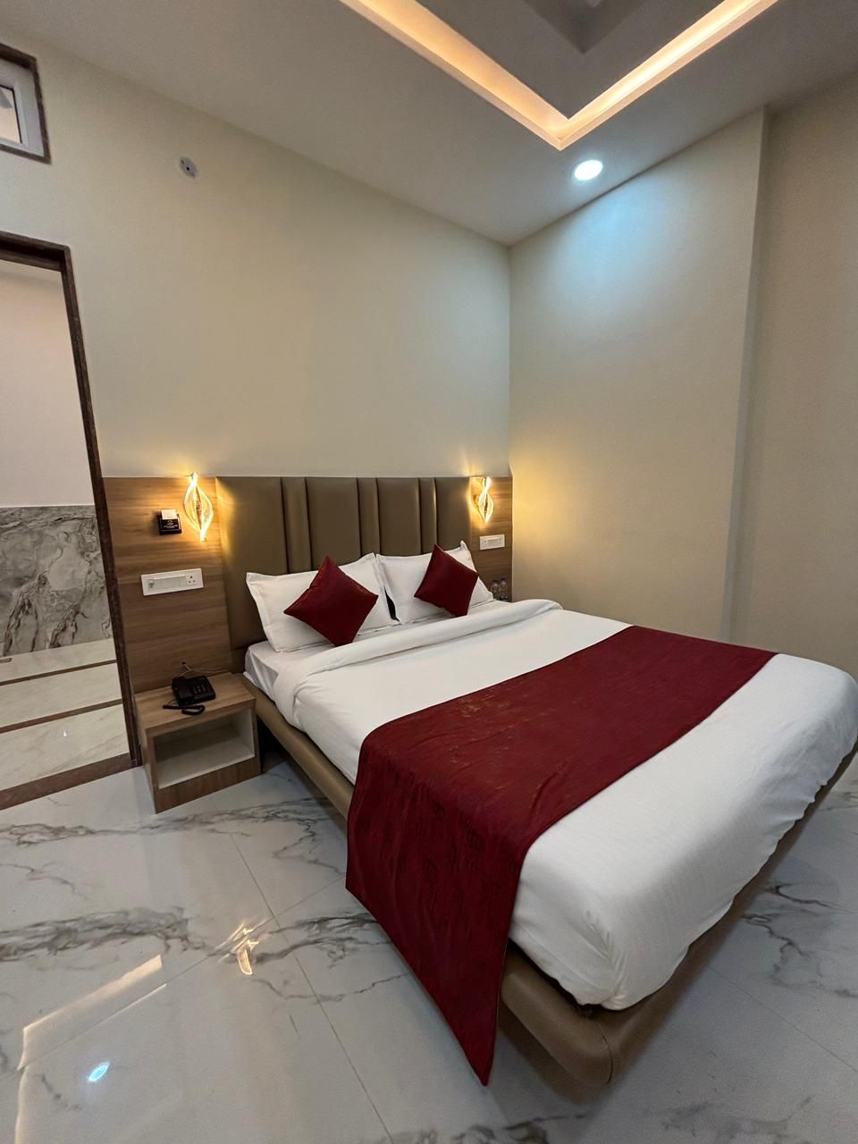 A modern hotel room with a large bed, marble flooring, and built-in nightstands.