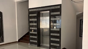 En rummelig lobby med en moderne elevator, marmorgulv og en trappe med trætrin.