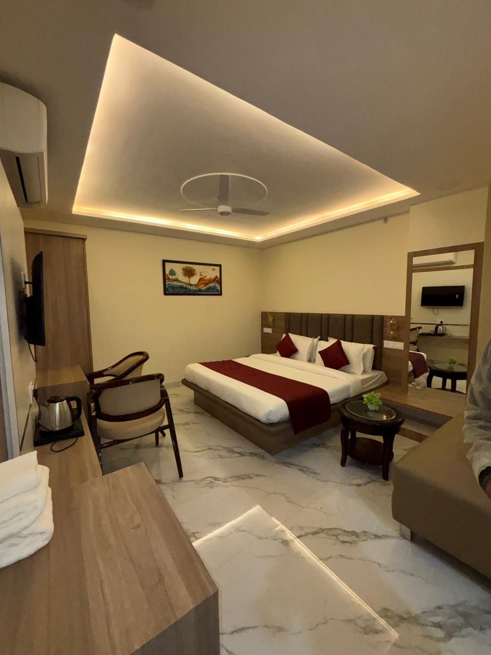A modern hotel room with a bed, a desk, a chair, a small table, and a sofa.