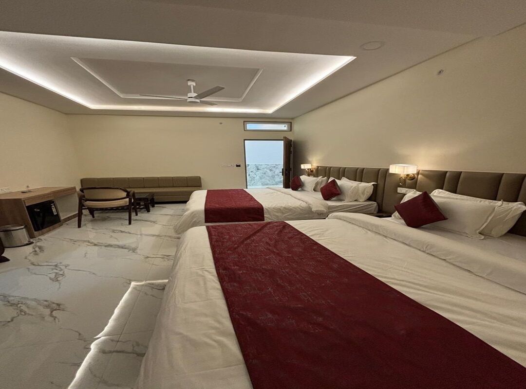 A hotel room with two beds, a desk, a chair, and a view of the outdoors.