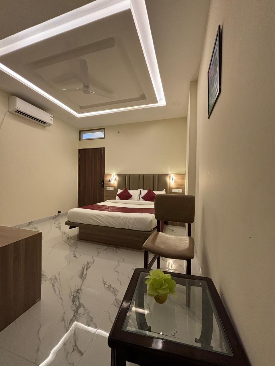 Une chambre d’hôtel moderne équipée d’un lit, de tables de chevet, d’un bureau et d’une table en verre agrémentée d’une fleur.