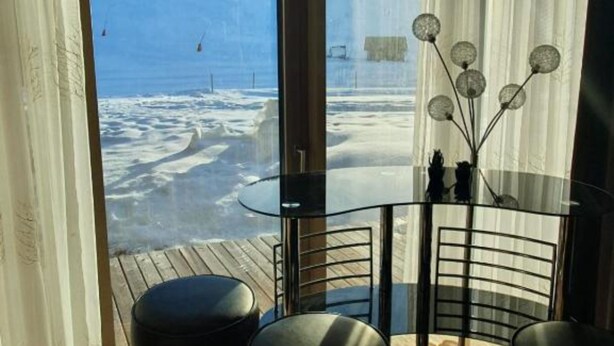 A room with a glass table and chairs, a view of a snowy landscape, and a decorative plant. - Apartment HAL (Hinterstoder)