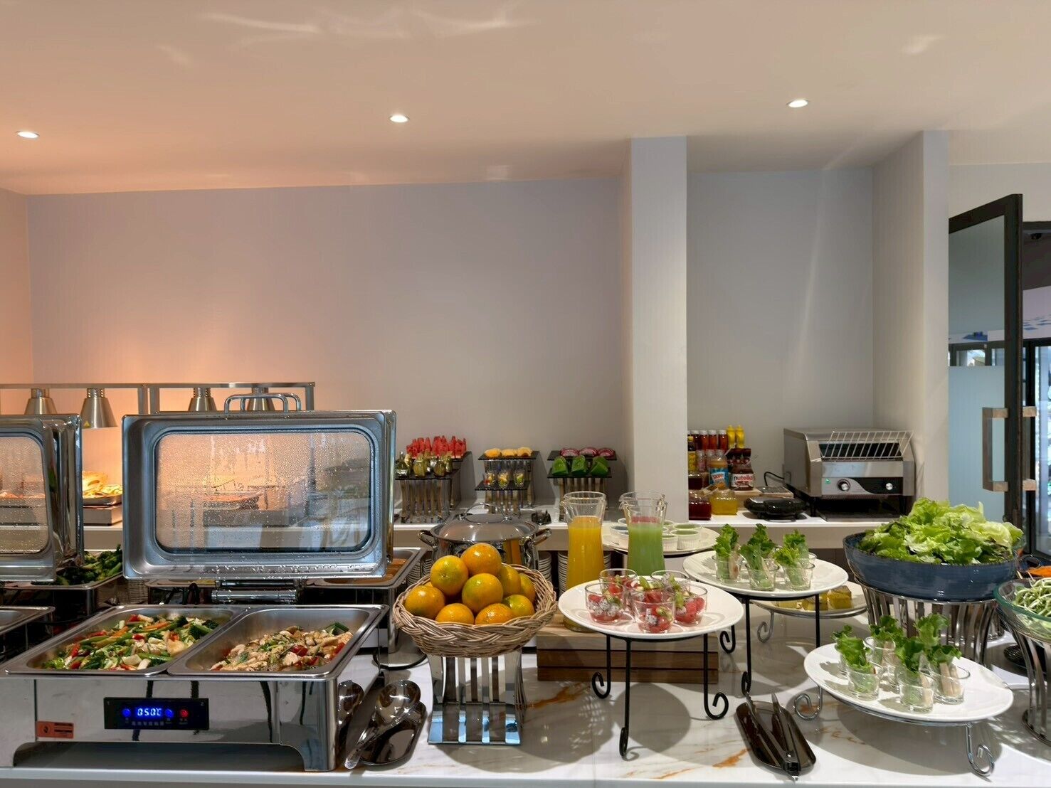 A buffet setup with various food items and beverages, including fruits, salads, and hot dishes.