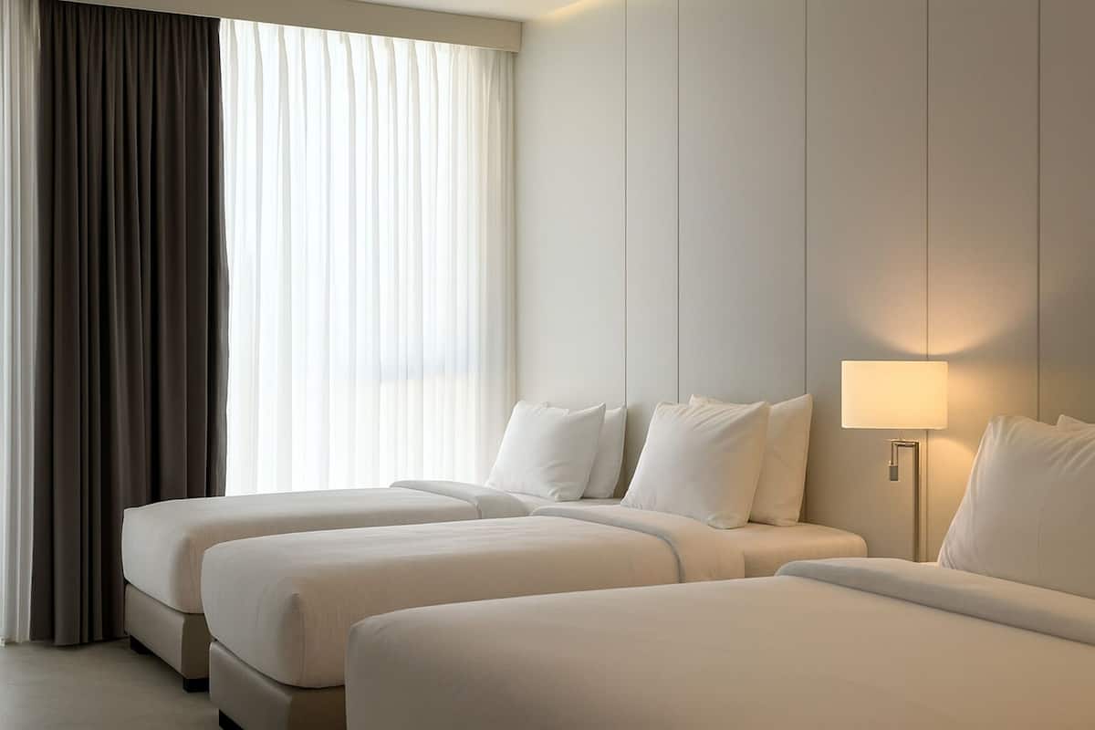 A hotel room with two beds, a bedside lamp, and a large window with curtains.