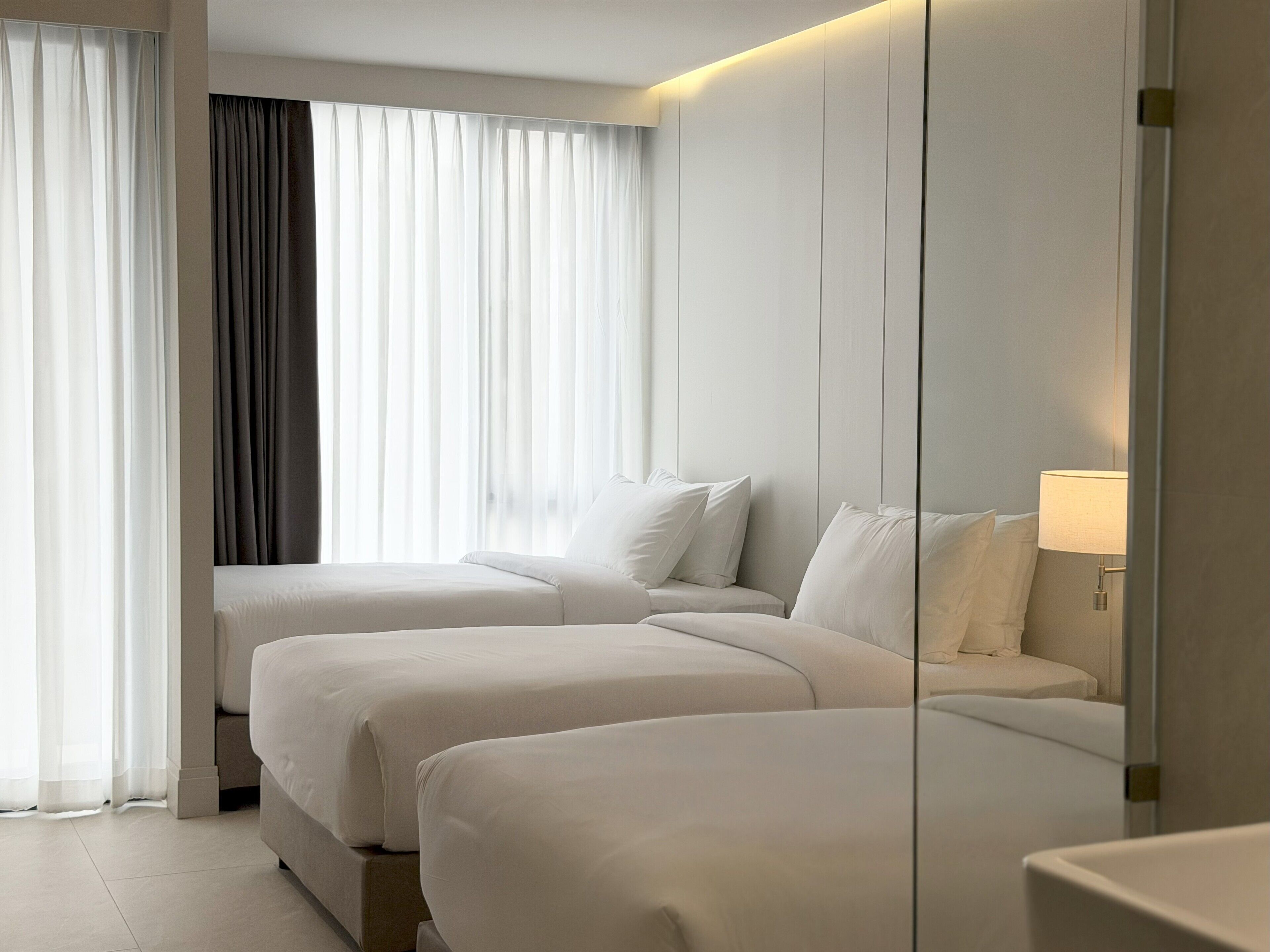 Une chambre d’hôtel avec deux lits, une grande fenêtre avec des rideaux légers et une lampe de chevet.