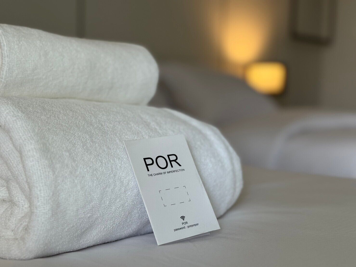 A neatly folded white towel with a POR card on a bed.