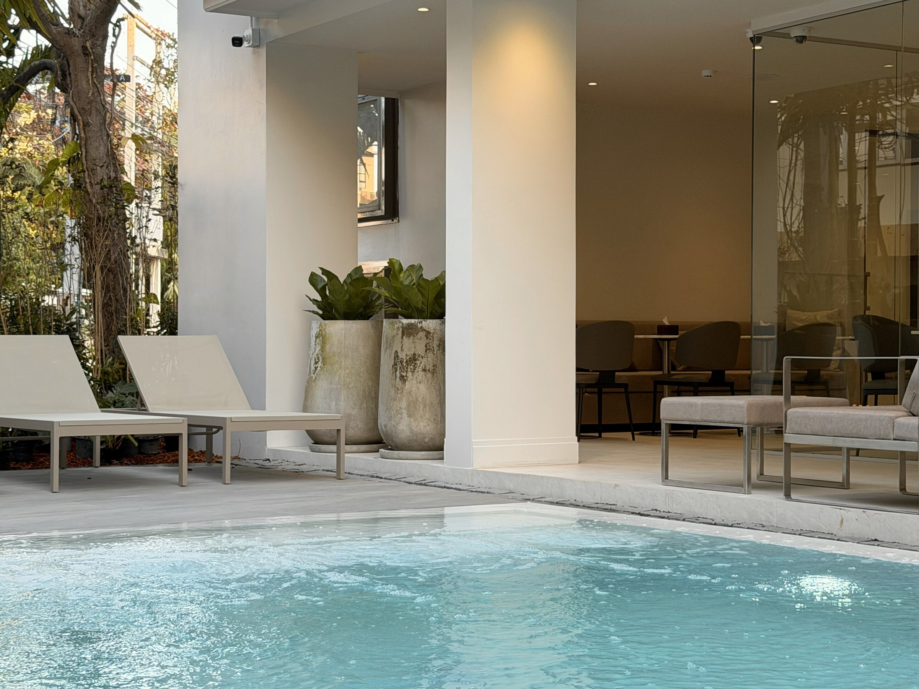 A modern indoor pool area with lounge chairs and seating, surrounded by large planters and a glass wall.
