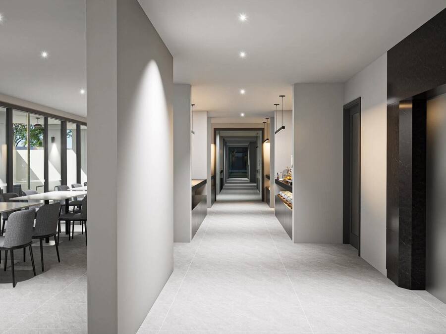 A modern hallway with a long table and chairs on the left, a dark wall on the right, and a staircase in the center.