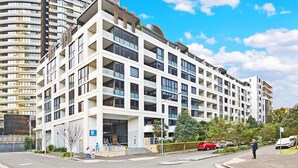 A modern multi-story residential building with balconies, large windows, and a flat roof. - Olympic Park Oasis | 2BR + Pool, Sauna & Parking (Sydney Olympic Park)