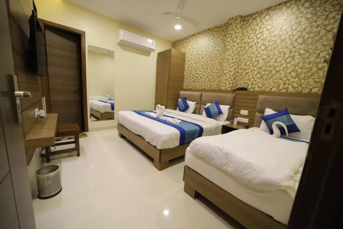 A hotel room with two beds, a wooden wardrobe, a small table, a trash bin, and an air conditioning unit.