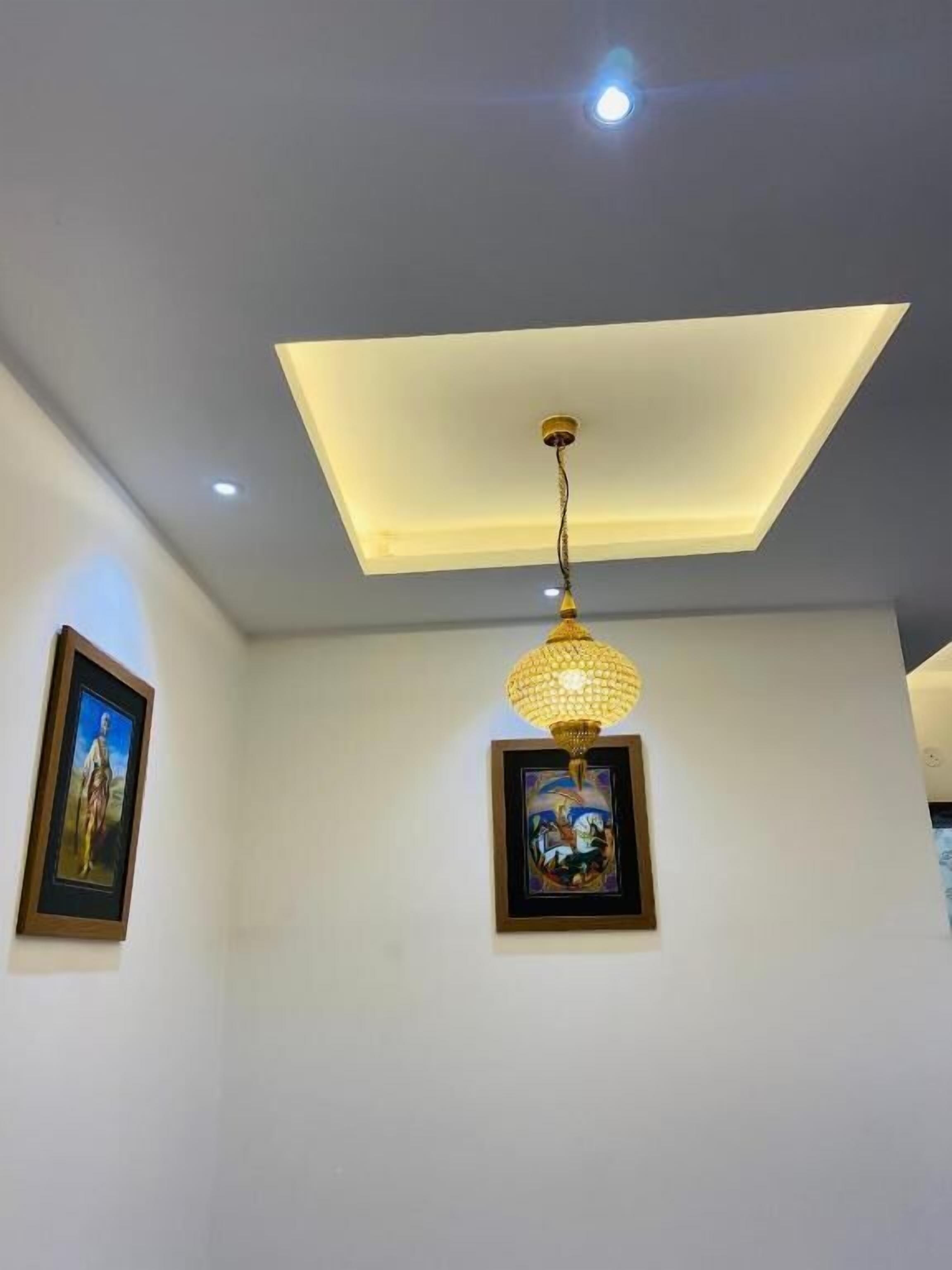 A room with a recessed ceiling light, a hanging pendant light, and two framed artworks on the walls.