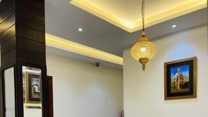 A modern hallway with a dark wooden accent wall, a white tiled floor, recessed ceiling lighting, and a framed picture on the wall. - Hotel SS Royal (Amritsar)