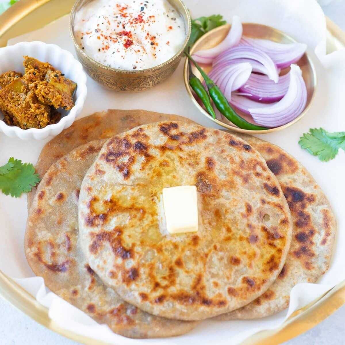 A plate with two pieces of flatbread, a small bowl of yogurt, sliced onions, and a bowl of chutney.
