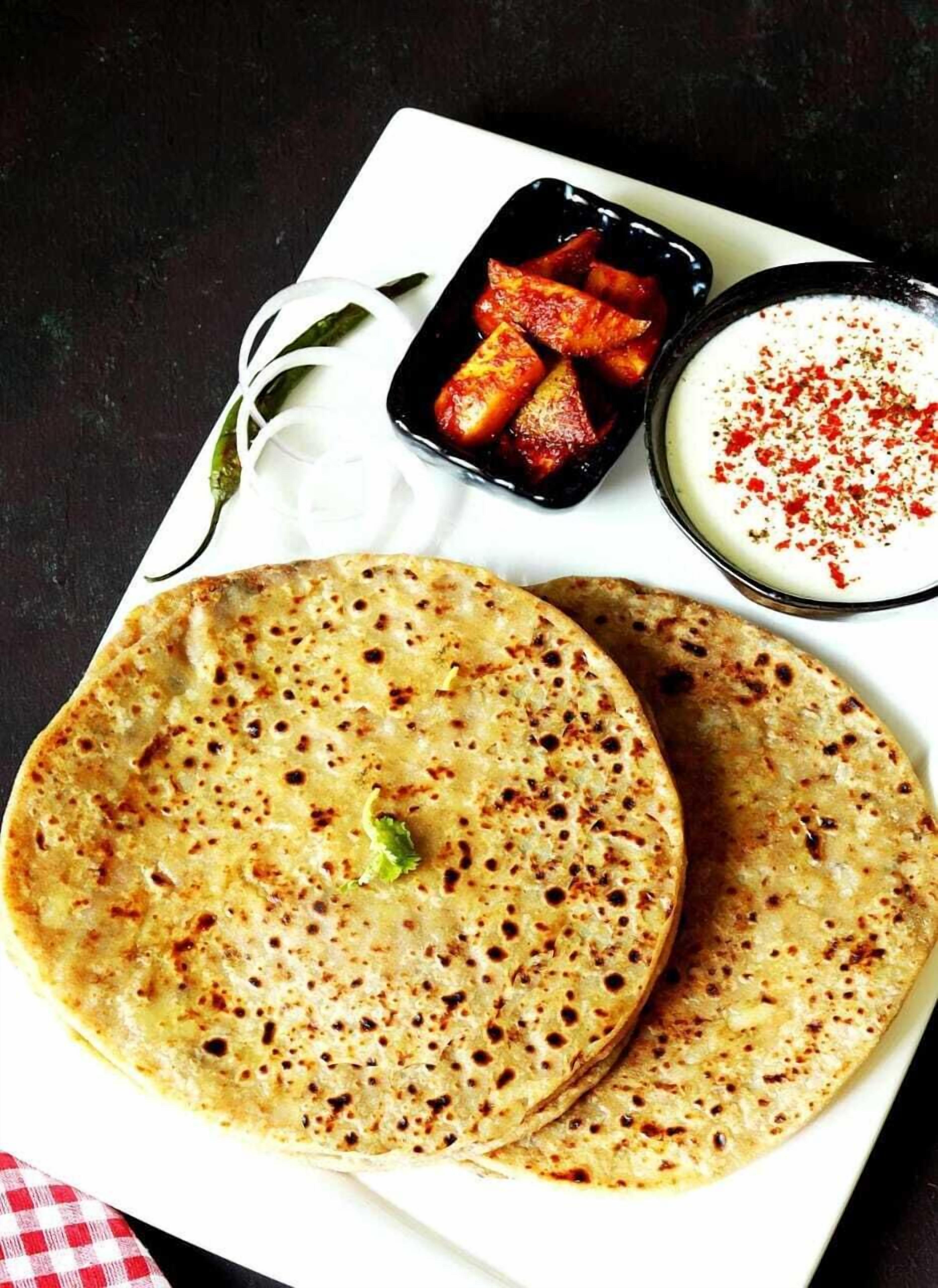 A plate with two flatbreads, a bowl of sliced tomatoes, and a bowl of white sauce with red seasoning.