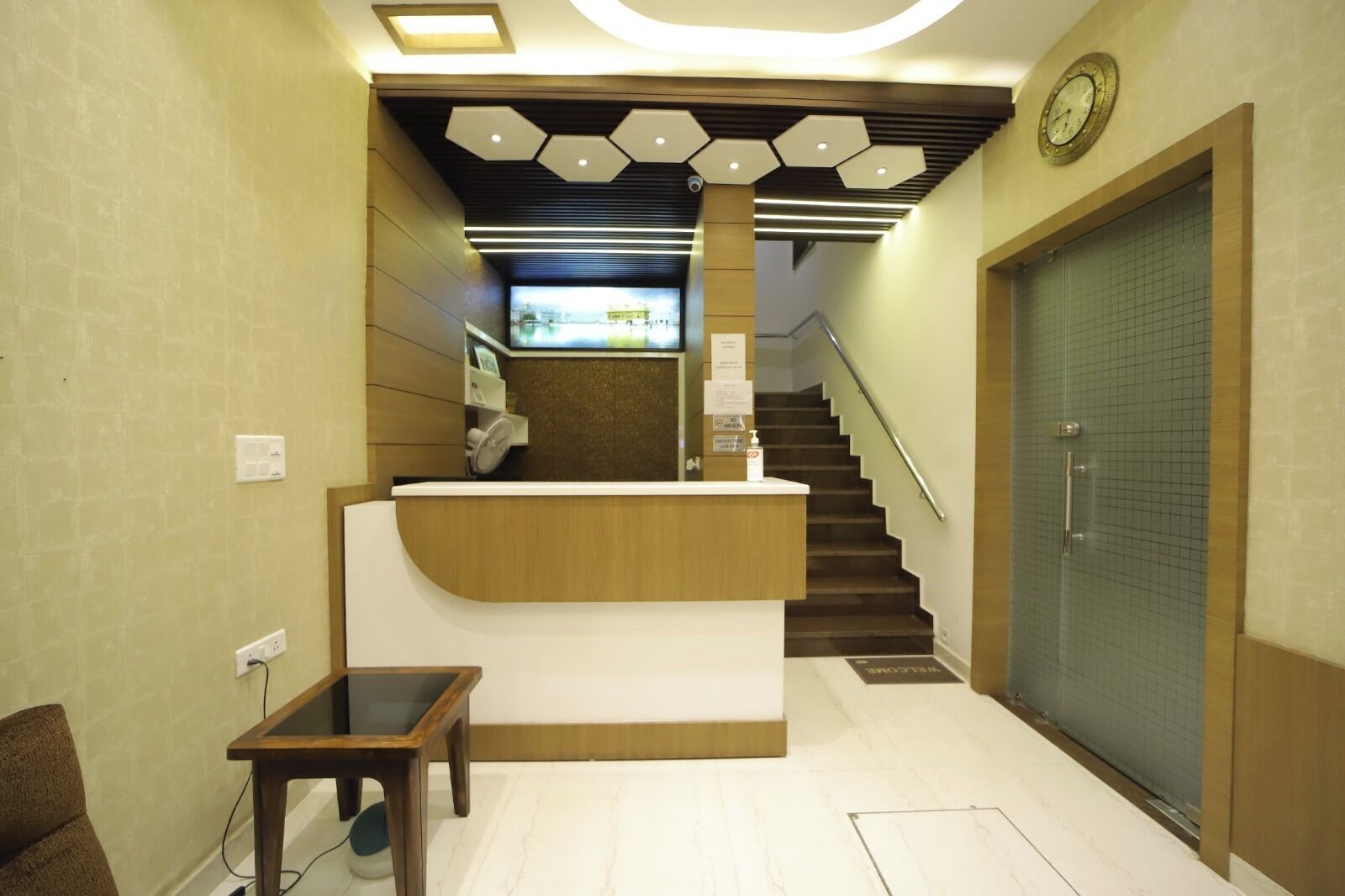 A reception area with a wooden reception desk, a small table, a staircase, and a door with a grid pattern.