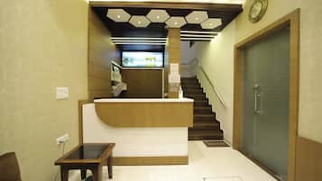 A reception area with a wooden reception desk, a small table, a staircase, and a door with a grid pattern.