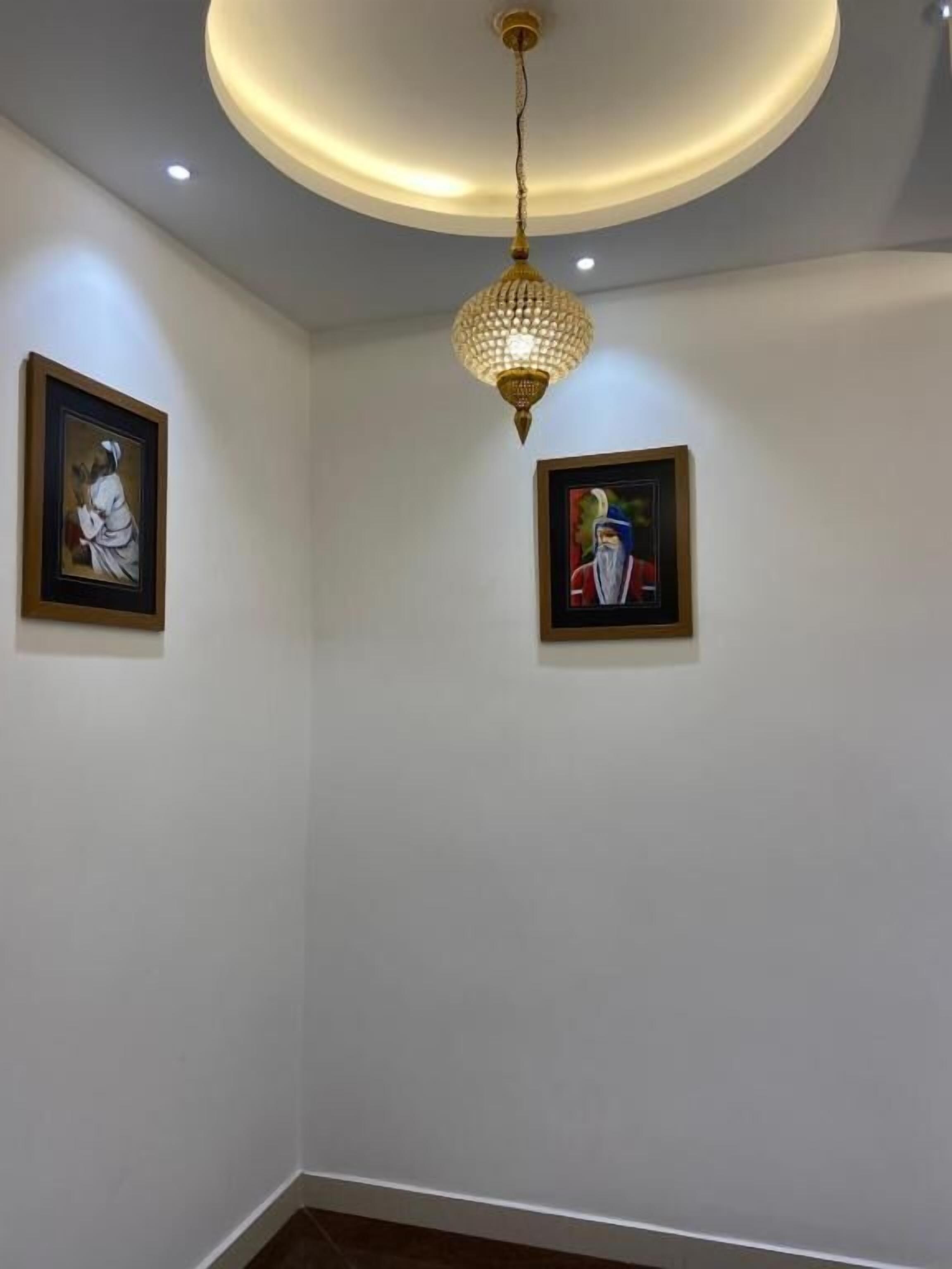 A room with white walls, two framed artworks, a modern chandelier, and recessed ceiling lighting.