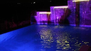 Une piscine avec des marches éclairées et des jeux d’eau, le tout illuminé la nuit.
