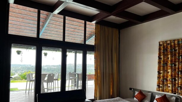 Une chambre avec une grande fenêtre, un lit, un banc et une vue sur l’extérieur.