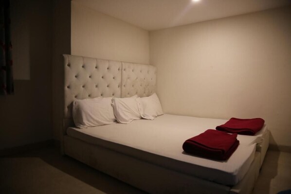 A single bed with a tufted headboard, white bedding, and two red blankets. - Champions Ranch (Hosur)
