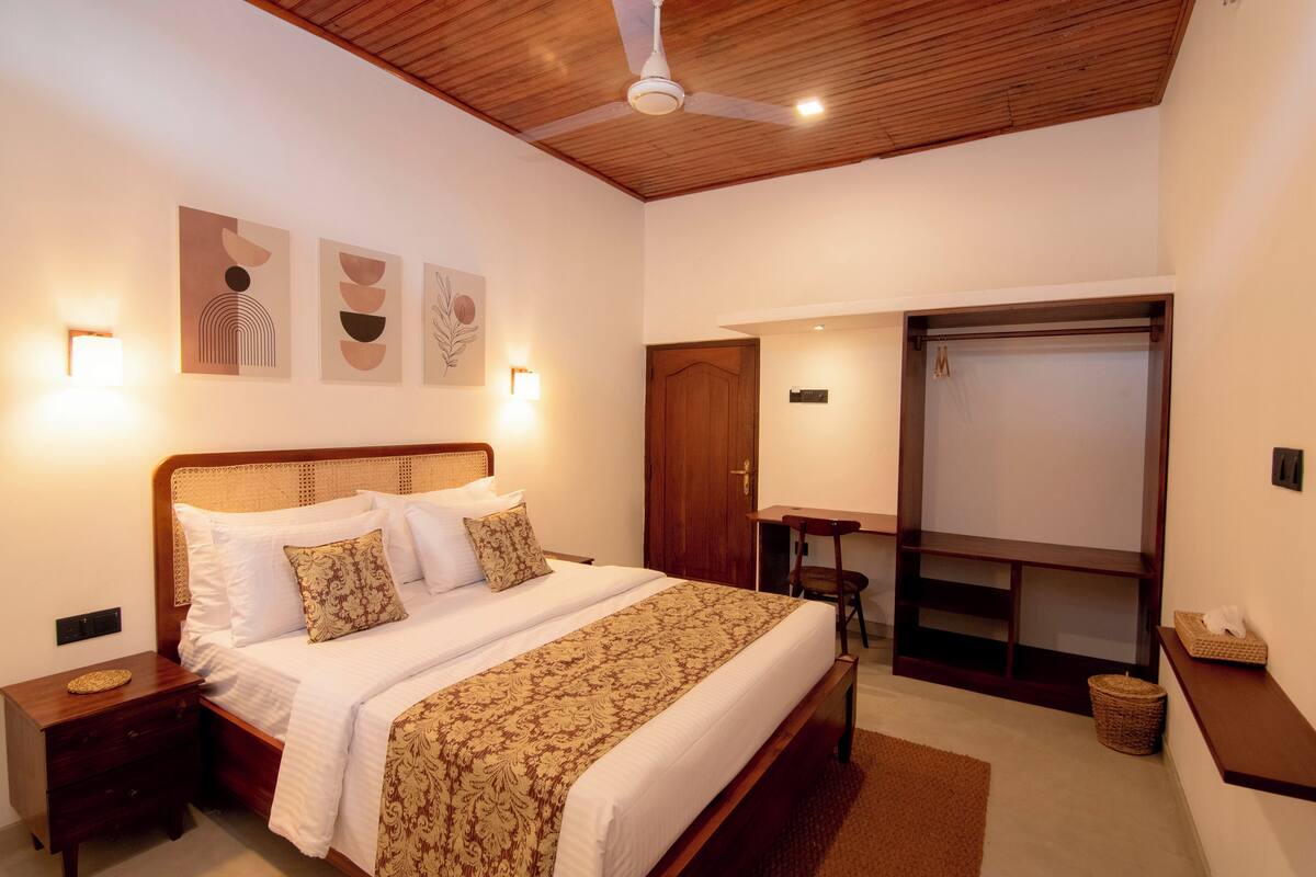 A bedroom with a wooden ceiling, a bed with patterned bedding, bedside tables, wall-mounted lights, and a wardrobe.
