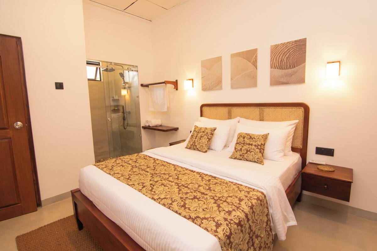 A bedroom with a large bed, a wooden nightstand, a glass shower enclosure, and wall-mounted artwork.