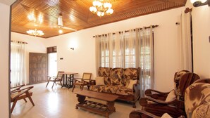 A spacious living room with a wooden ceiling, a patterned sofa, a coffee table, and a dining area with chairs and a table. - Sand Cliff Villa (Galle)