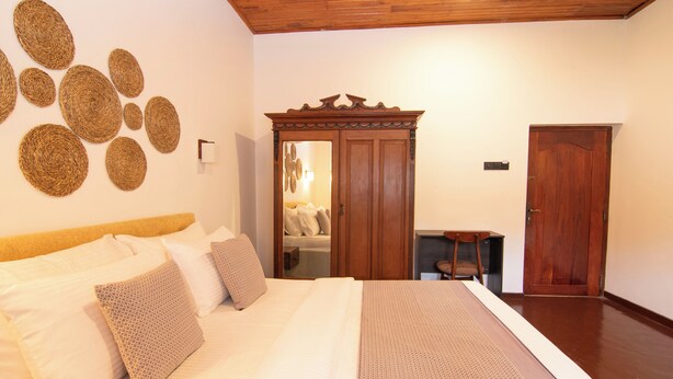 A bedroom with a bed, pillows, a wooden wardrobe, and a mirror. - Sand Cliff Villa (Galle)