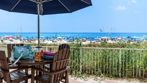 A patio table with chairs, a large umbrella, and a view of a crowded beach with numerous umbrellas and people. - Beachfront Condo, Oceanview Balcony, Lagoon Pool | Thomas Dr #2308 by AvantStay (Panama City)