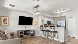 A modern living room with a flat-screen TV, a sofa, and a kitchen area with a bar stool set. - Beachfront Condo, Oceanview Balcony, Lagoon Pool | Thomas Dr #2308 by AvantStay (Panama City)