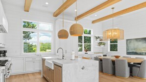 Una cocina moderna con armarios blancos, una isla grande y una zona de comedor con sillas grises.