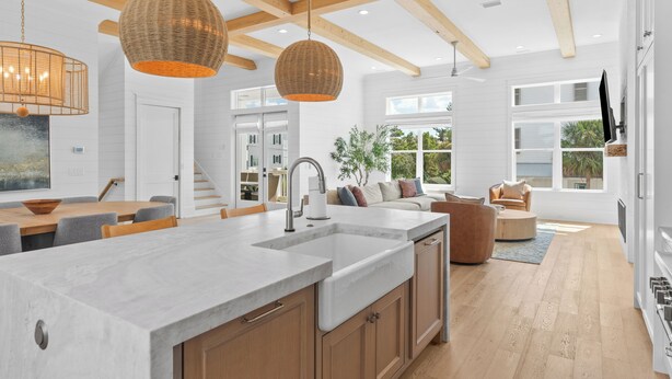 Una cocina moderna con una isla grande, vigas de madera e iluminación colgante.
