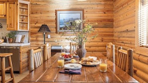 Ein Holzblockhaus-Interieur mit einem Esstisch, der für ein Frühstück gedeckt ist, inklusive Tellern, Gläsern und einer Blumenvase.