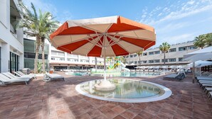 A pool area with lounge chairs, a central fountain, and a large umbrella. - Estival Park Marena (Vila-Seca)