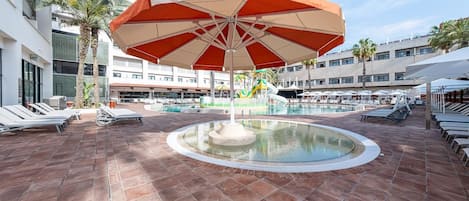 A pool area with lounge chairs, a central fountain, and a large umbrella.