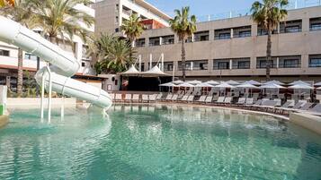 A swimming pool with a water slide, lounge chairs, and palm trees.