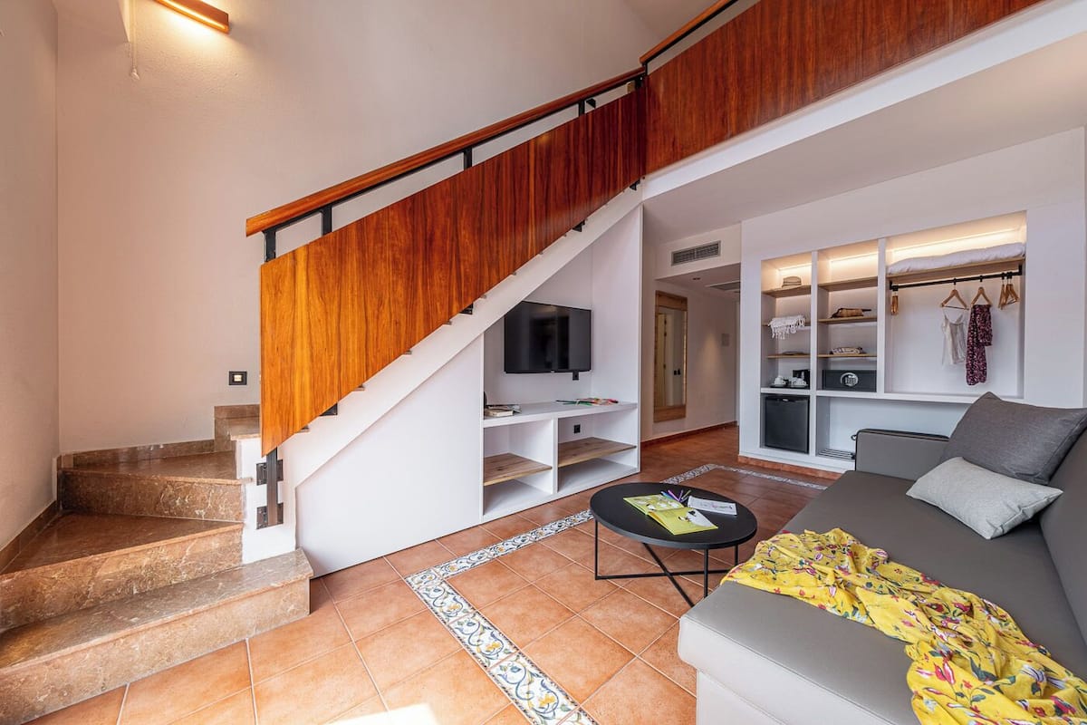 A modern living room with a wooden staircase, a flat-screen TV, a sofa, and a dining area.