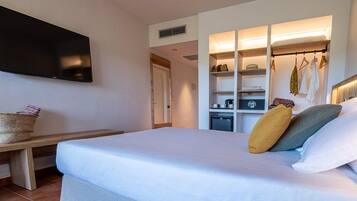 Habitación de hotel con cama, televisión montada en la pared, banco de madera, armario empotrado con estantes y una pequeña cocina.