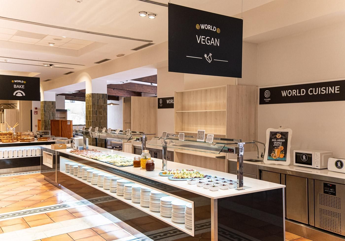 A modern food display area with various vegan and non-vegan options, including a juice dispenser and a microwave.