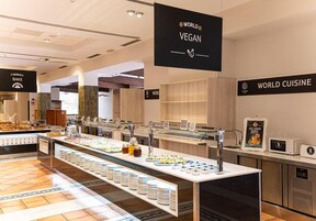 Un espacio moderno para exhibir alimentos con diversas opciones veganas y no veganas, que incluye un dispensador de zumos y un microondas.