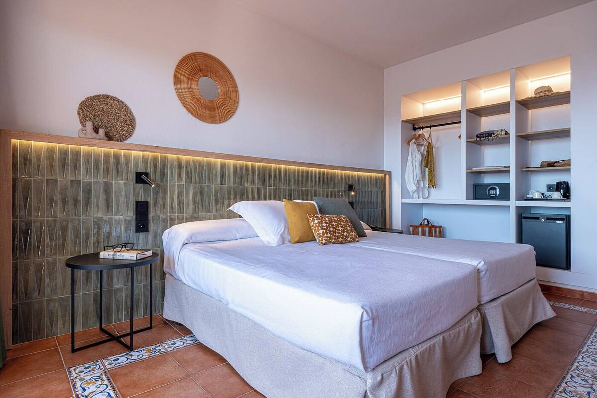 A modern bedroom with a large bed, bedside tables, a built-in wardrobe, and a small kitchenette.