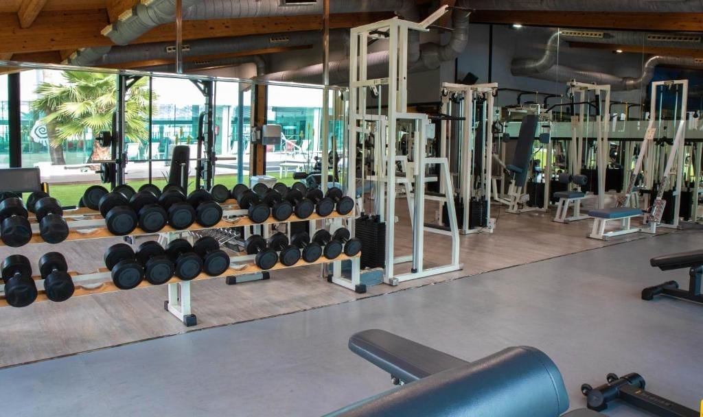 Un gimnasio con equipo de levantamiento de pesas, bancos y mancuernas.