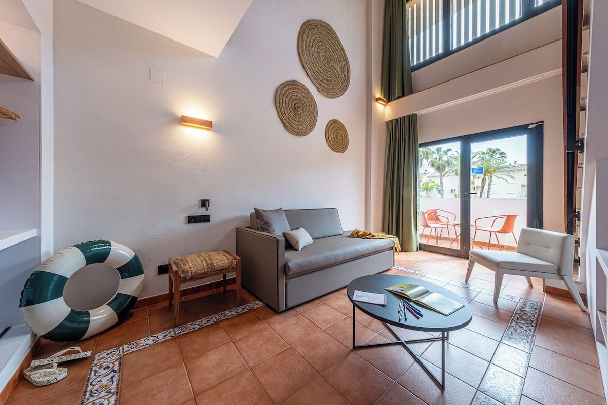 A modern living room with a grey sofa, a small wooden stool, a round coffee table, and a large decorative cushion.